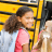 Young girl wearing a backpack smiles while stepping onto a yellow school bus.