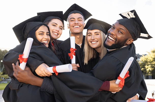 Graduating military-connected students in caps and gowns holding diplomas and hugging, highlighting the USBA Dietrich Memorial Scholarship for college financial aid.