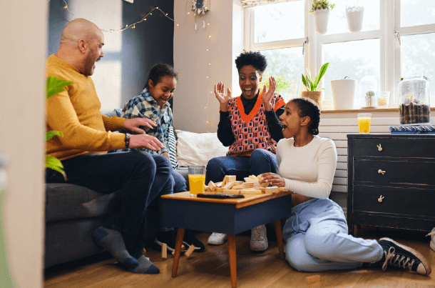 Family members laugh and play a game together in their living room, reflecting the loved ones military and federal families work to protect through life insurance.