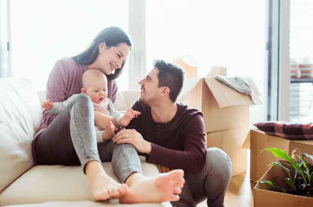 New parents smiling with their baby in a living room, symbolizing protecting loved ones with term life insurance during important life stages.