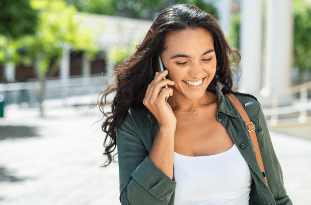 Young woman smiling while talking on her phone outdoors, discussing whole life insurance options for long-term financial protection.