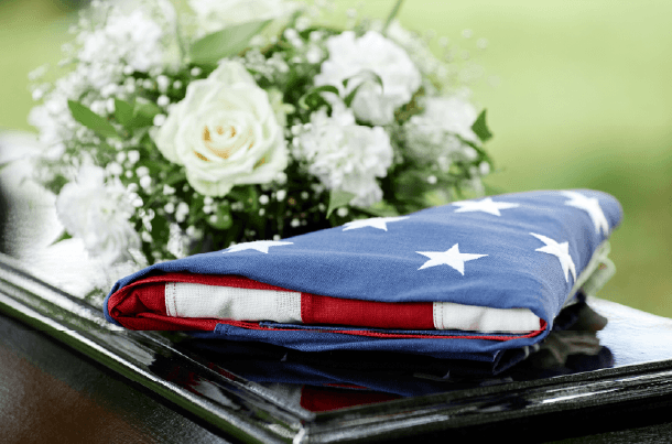 Folded U.S. flag resting on a casket beside white funeral flowers, representing burial and final-expense planning for Veterans and military families.