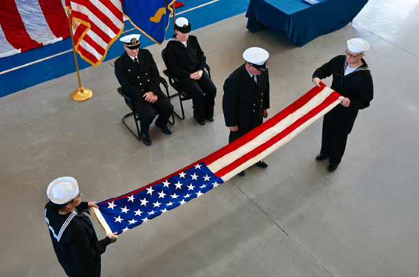 U.S. Navy sailors ceremonially fold an American flag as uniformed service members look on.
